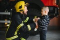 Portrait of rescued little boy with firefighter man standing near fire truck. Firefighter in fire fighting operation. Royalty Free Stock Photo