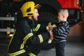 Portrait of rescued little boy with firefighter man standing near fire truck. Firefighter in fire fighting operation.