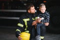 Portrait of rescued little boy with firefighter man standing near fire truck. Firefighter in fire fighting operation. Royalty Free Stock Photo