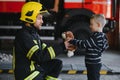 Portrait of rescued little boy with firefighter man standing near fire truck. Firefighter in fire fighting operation.