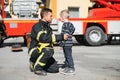 Portrait of rescued little boy with firefighter man standing near fire truck. Firefighter in fire fighting operation. Royalty Free Stock Photo