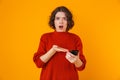 Portrait of resentful woman holding and using cell phone while standing isolated over yellow background Royalty Free Stock Photo