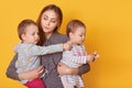 Portrait of responsible attentive mother spending time with her little children, holding twin girls in arms, listening to them