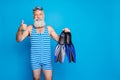 Portrait of retired grandfather with white hairstyle holding diving equipment wearing striped costume isolated over blue Royalty Free Stock Photo