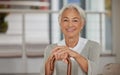 Portrait of a retired senior woman holding a wooden cane and smiling while sitting at home. Happy old lady leaning on a Royalty Free Stock Photo
