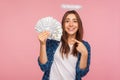 Portrait of rich angelic girl, lottery winner with halo over head pointing money and smiling happily Royalty Free Stock Photo