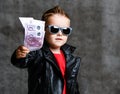 Portrait of rich kid boy in sunglasses and leather jacket handing us a bundle of money euro cash, donating giving