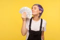 Portrait of rich stylish hipster girl smelling money and closing eyes in pleasure. yellow background, studio shot