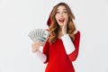 Portrait of rich woman 20s wearing Santa Claus red costume smiling and holding fan of money in dollar banknotes, isolated over Royalty Free Stock Photo