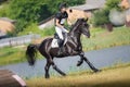 Rider man and black stallion horse galloping fast near lake during eventing cross country competition Royalty Free Stock Photo