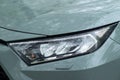 A portrait of the right headlight of a green hybrid toyota rav4 car with water drops. Kyiv, Ukraine - April 2024.