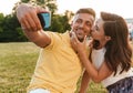 Portrait of romantic adult couple kissing and taking selfie photo on cellphone while sitting on grass in park Royalty Free Stock Photo
