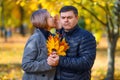 Portrait of romantic couple in autumn city park, woman whispers bad news to man, and he is very unhappy, yellow leaves and bright