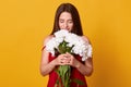 Portrait of romantic elegant brunette closing her eyes, feeling smell of flowers, holding bouquet of white peonies, standing
