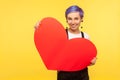 Portrait of romantic stylish hipster girl holding big paper heart and smiling. yellow background, studio shot