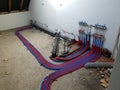A portrait of a room under construction with a central heating collector on the wall. The warm and cold water tubes are running