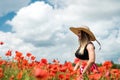 portrait of rpetty ukrainian woman in black top and hat with big bouquet of poppies in field