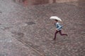 Portrait of running boy with umbrella on cobbles place in the city