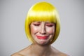 Portrait of sad alone cute young woman with freckles, red makeup and yellow wig, crying and depressed