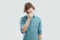 Portrait of sad alone handsome long haired blonde young man in blue casual shirt standing, holding his head down and crying Royalty Free Stock Photo