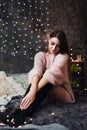 Portrait of sad attractive young woman with tinsel confetti and garland lights celebrating alonein dark room. New year`s Royalty Free Stock Photo