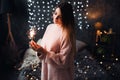 Portrait of sad attractive young woman with tinsel confetti and garland lights celebrating alonein dark room. New year`s Royalty Free Stock Photo