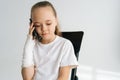 Portrait of sad blonde little girl with broken arm wrapped in plaster bandage talking smartphone, smiling looking down Royalty Free Stock Photo