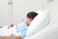 Portrait of sad child looking at camera lying in bed in hospital room on white background with copy space
