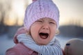 Portrait of a sad crying blonde little girl in a pink knitted hat and a knitted scarf. Royalty Free Stock Photo