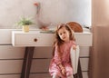 Portrait of sad little girl in domestic interior. Cute blonde female child having bored and upset look, sitting on wooden chair Royalty Free Stock Photo