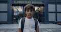 Sad elementary age boy near modern school entrance. Teen student looking camera. Royalty Free Stock Photo