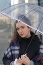 Portrait of sad girl in autumn coat under transparent umbrella. Charming young curly woman use umbrella in rainy day Royalty Free Stock Photo