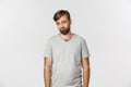 Portrait of sad and gloomy bearded man in gray t-shirt, frowning and looking miserable, standing over white background