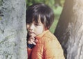 Portrait of sad kid standing next to big tree, Lonely child standing alone and looking down with thinking face in the park,Little Royalty Free Stock Photo