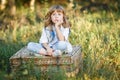 A portrait of a sad little boy with blue eyes and long blond hair sitting on a basket outside at sunset Royalty Free Stock Photo