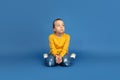 Portrait of sad little girl sitting on blue studio background, autism concept