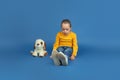 Portrait of sad little girl sitting on blue studio background, autism concept