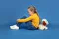Portrait of sad little girl sitting on blue studio background, autism concept Royalty Free Stock Photo