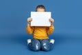 Portrait of sad little girl sitting on blue studio background, autism concept