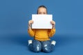 Portrait of sad little girl sitting on blue studio background, autism concept