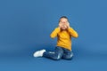 Portrait of sad little girl sitting on blue studio background, autism concept