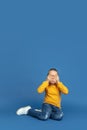 Portrait of sad little girl sitting on blue studio background, autism concept