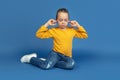 Portrait of sad little girl sitting on blue studio background, autism concept