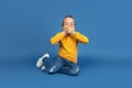 Portrait of sad little girl sitting on blue studio background, autism concept