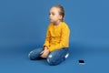 Portrait of sad little girl sitting on blue studio background, autism concept