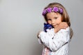 Portrait of sad little girl in white dress and purple wreath with plush unicorn toy on gray isolated background. Royalty Free Stock Photo