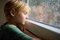 Portrait of a sad preteen boy standing at the window. Child watching the rain outside. Post-traumatic disorder. Accommodation of Royalty Free Stock Photo