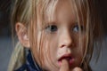 Portrait of a sad romantic little girl with big blue eyes and a finger in her mouth from Eastern Europe, close-up, dark background Royalty Free Stock Photo