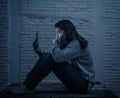 Young sad woman alone looking at smart phone in fear suffering Internet harassment and cyberbullying