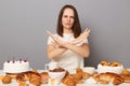 Portrait of sad serious woman with brown hair sitting at table full of pastry, showing no way gesture, crossed arms, saying do not Royalty Free Stock Photo